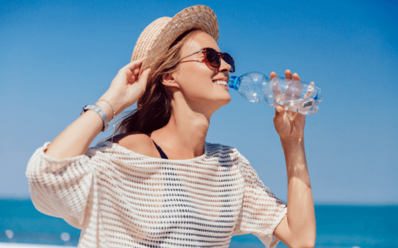 mujer playa sombrero bebiendo agua hidratacion cabello puntas abiertas cursos de peluqueria en parla-academia-peluqueria-estetica.com
